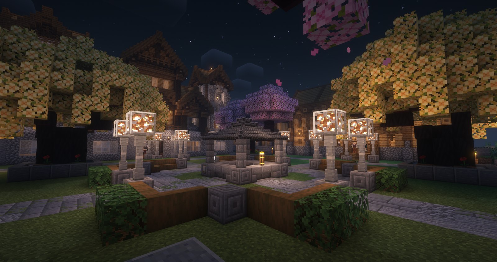 A lantern-lit Minecraft village courtyard with flowering trees, timber houses and a stone pavilion at night
